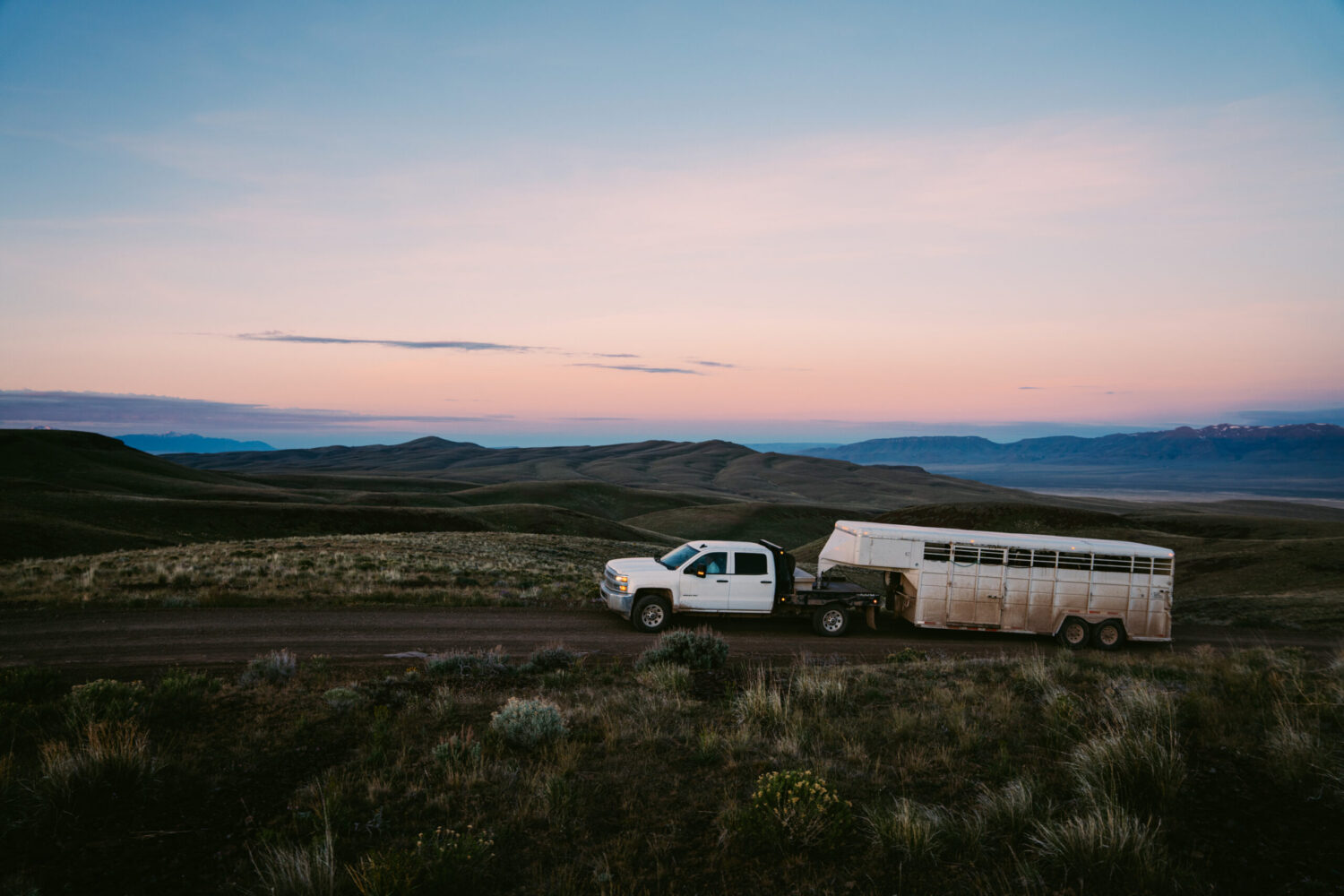 Pickup truck hauling trailer on ranch road at sunset