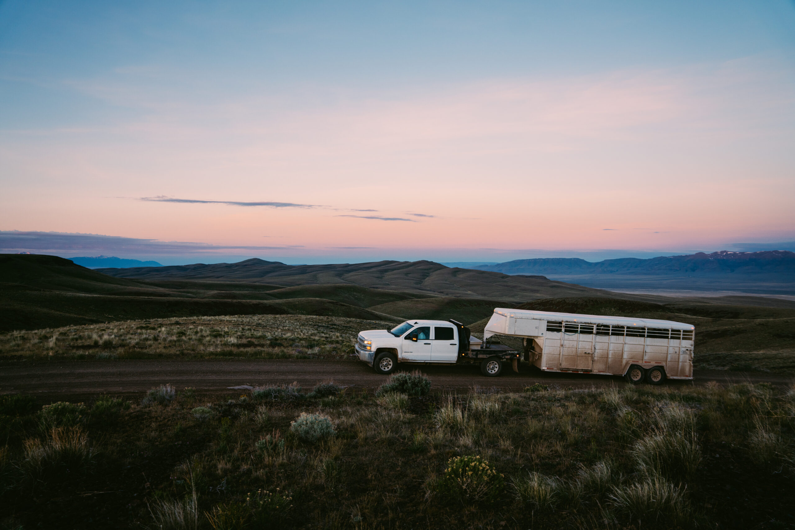 Pickup truck hauling trailer on ranch road at sunset